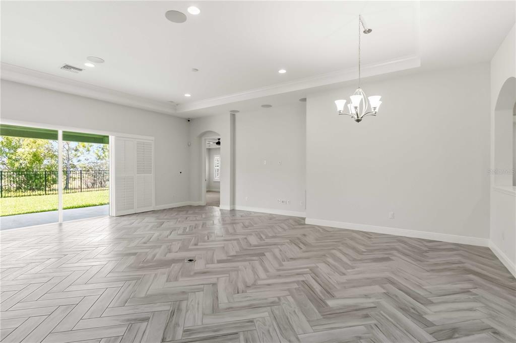 A bright, empty living room features light-colored herringbone flooring, a tray ceiling, and sliding doors — 6404 MAIDEN SEA DRIVE, APOLLO BEACH, FL