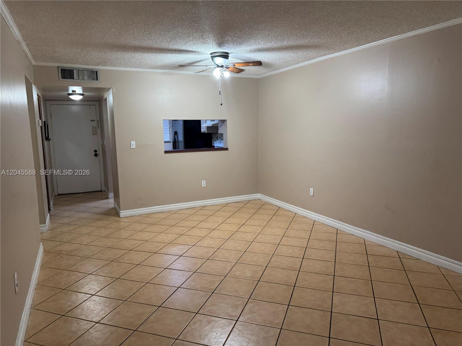 An empty living room features beige walls, tan tile flooring, and a kitchen pass-through window — 10865 SW 112th Ave # 105, Miami FL 33176, MIAMI, FL