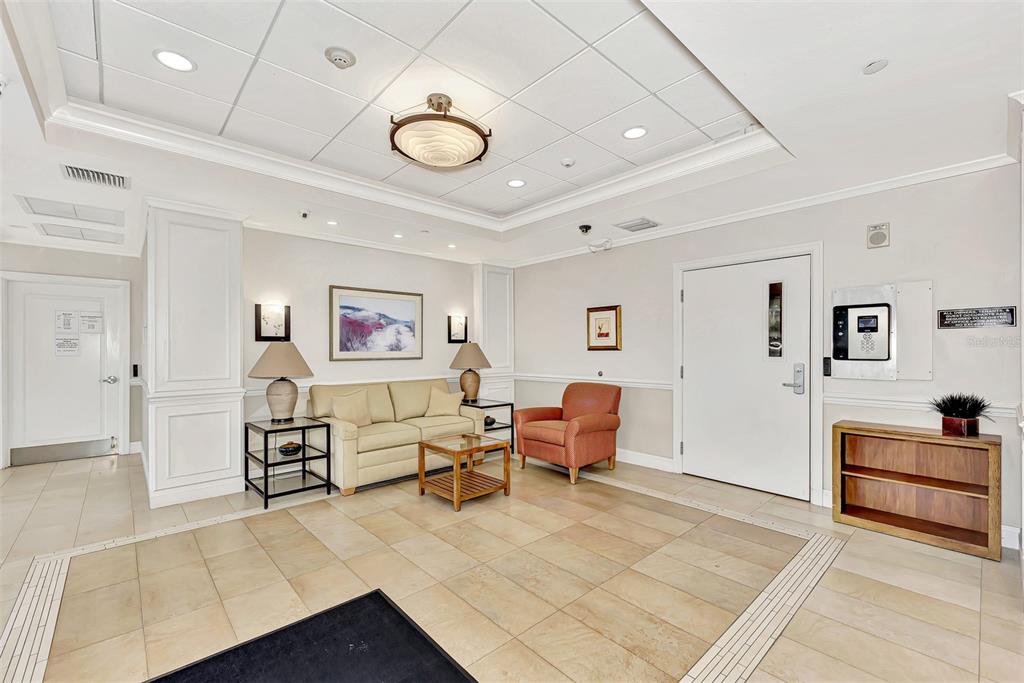 A lobby features a beige sofa, an orange armchair, tile flooring, and a coffered ceiling — 631 ALHAMBRA ROAD UNIT 1004, VENICE, FL