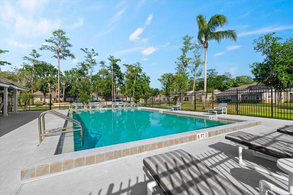 An outdoor swimming pool with a tiled edge is surrounded by lounge chairs and fencing — 102 BOB WHITE COURT UNIT 102C, DAYTONA BEACH, FL