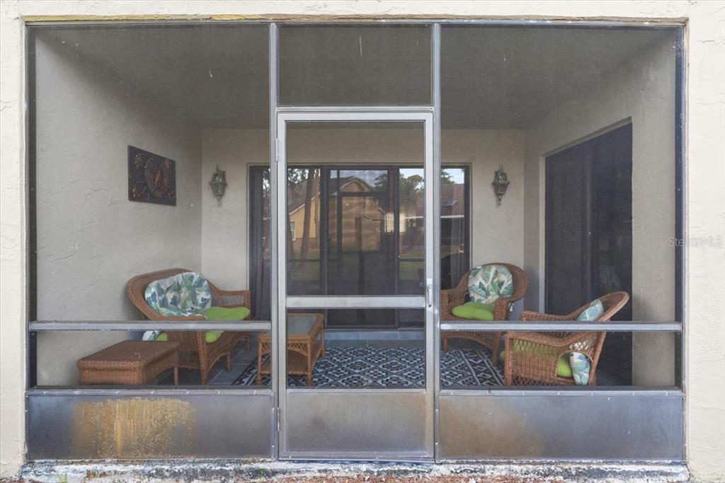 A screened-in patio features wicker furniture with green cushions and a patterned area rug — 102 BOB WHITE COURT UNIT 102C, DAYTONA BEACH, FL