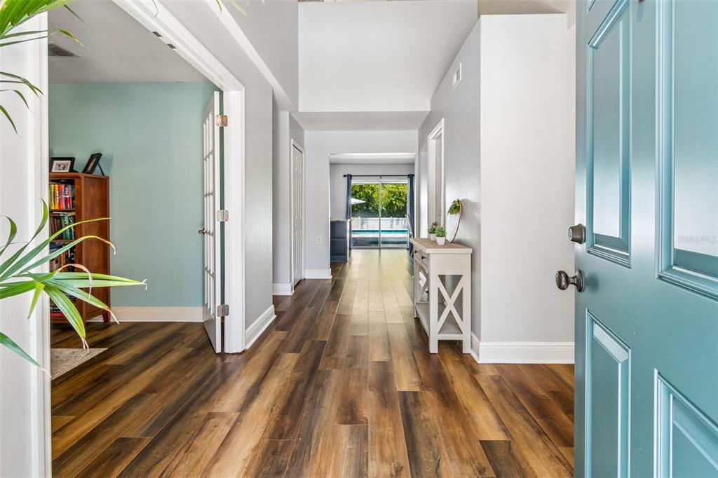 A view from an open teal door into a hallway with wood-look flooring and pool — 3216 BELLERICAY LANE, LAND O LAKES, FL