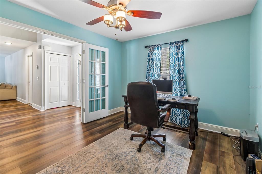 A home office features light blue walls, wood-look flooring, a desk, and French doors — 3216 BELLERICAY LANE, LAND O LAKES, FL