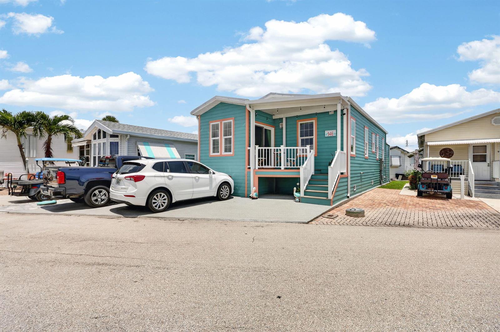 A teal mobile home with a white porch and driveway sits under a cloudy sky — 946 Nettles Boulevard, Jensen Beach FL 34957, JENSEN BEACH, FL
