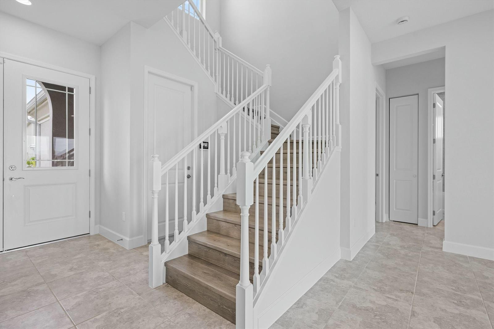 A bright entryway features a wooden staircase with white railings and light-colored tile flooring — 14964 Redcove Place, Westlake FL 33470, WESTLAKE, FL