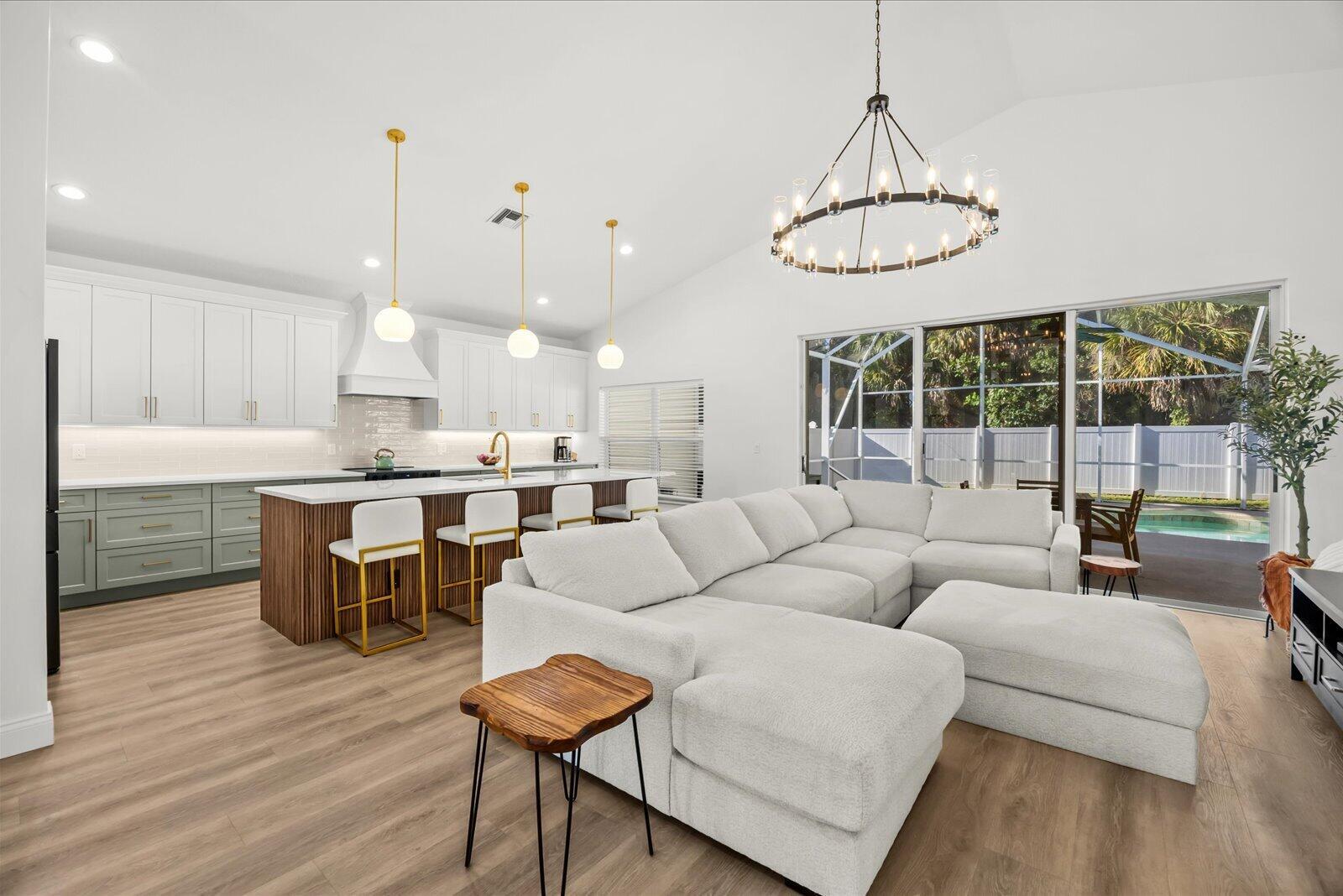A modern open-concept kitchen and living area with white cabinets, a wood-slatted island, and pool view — 110 Pennock Trace Drive, Jupiter FL 33458, JUPITER, FL