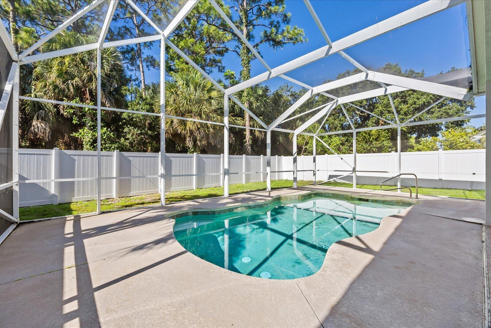 A swimming pool with a screen enclosure sits in a backyard with a white fence — 110 Pennock Trace Drive, Jupiter FL 33458, JUPITER, FL