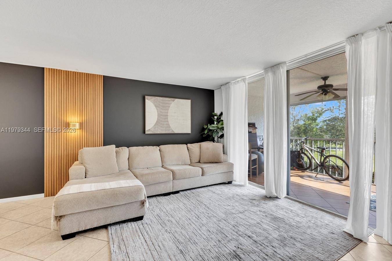A living room features a beige sectional sofa, a gray area rug, and wood-slat paneling — 4550 NW 18th Ave # 206, Deerfield Beach FL 33064, DEERFIELD BEACH, FL