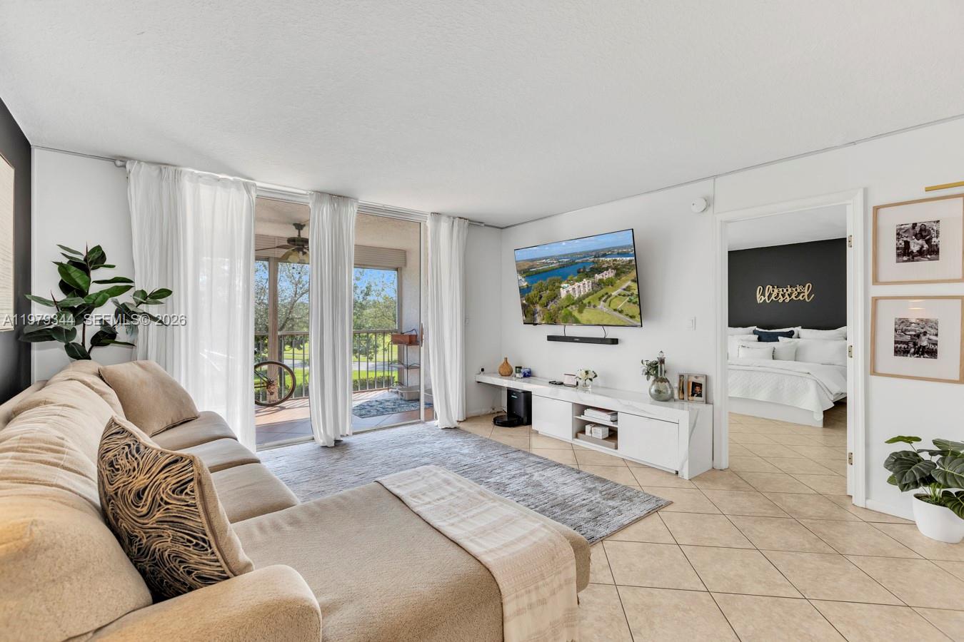 A living room features a beige sectional sofa, a wall-mounted television, and a balcony view — 4550 NW 18th Ave # 206, Deerfield Beach FL 33064, DEERFIELD BEACH, FL