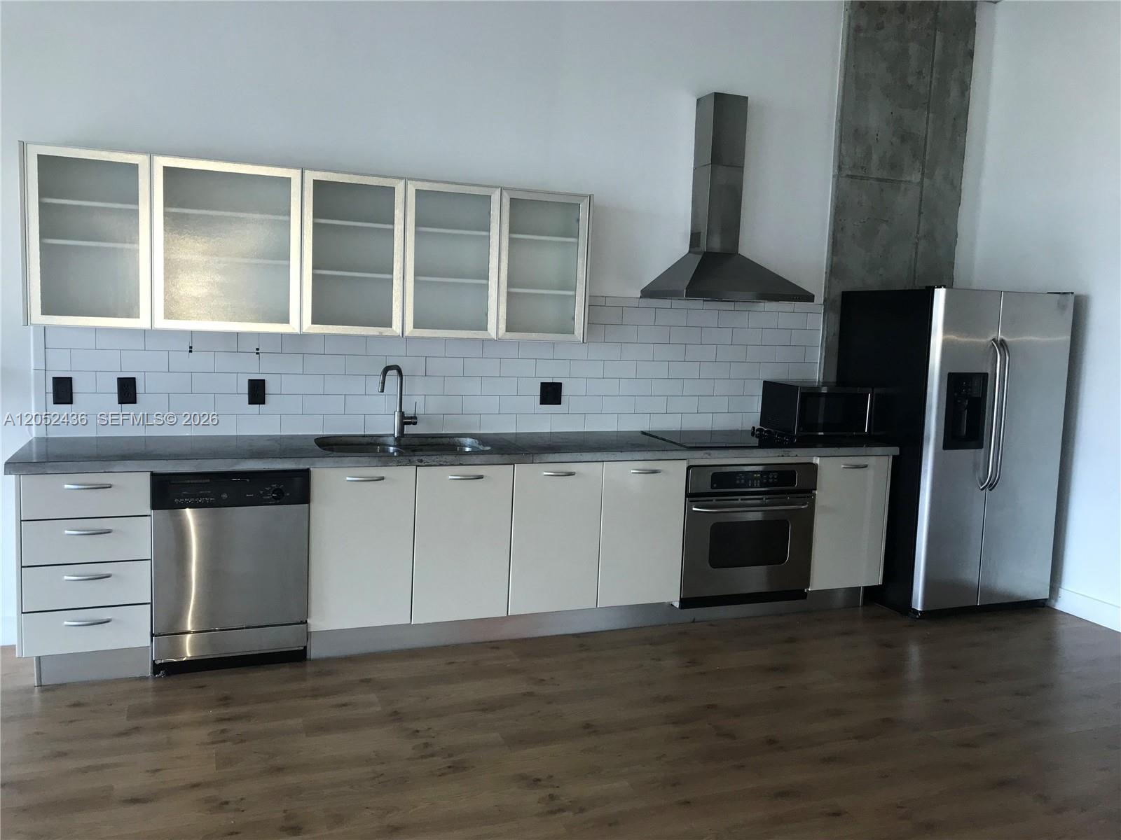 A modern kitchen features white cabinets, stainless steel appliances, a subway tile backsplash, and wood flooring — 1749 NE Miami Ct # 413, Miami FL 33132, MIAMI, FL