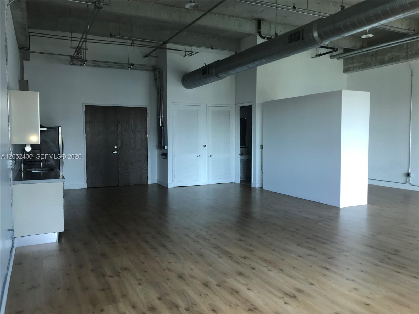 An open-concept room features wood-look flooring, exposed industrial ductwork, and a small kitchen area — 1749 NE Miami Ct # 413, Miami FL 33132, MIAMI, FL