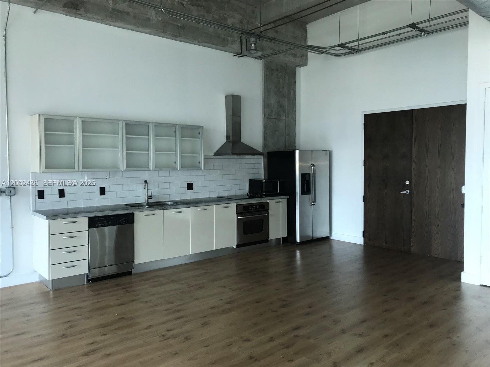A modern kitchen features white cabinets, stainless steel appliances, and exposed concrete ceilings — 1749 NE Miami Ct # 413, Miami FL 33132, MIAMI, FL