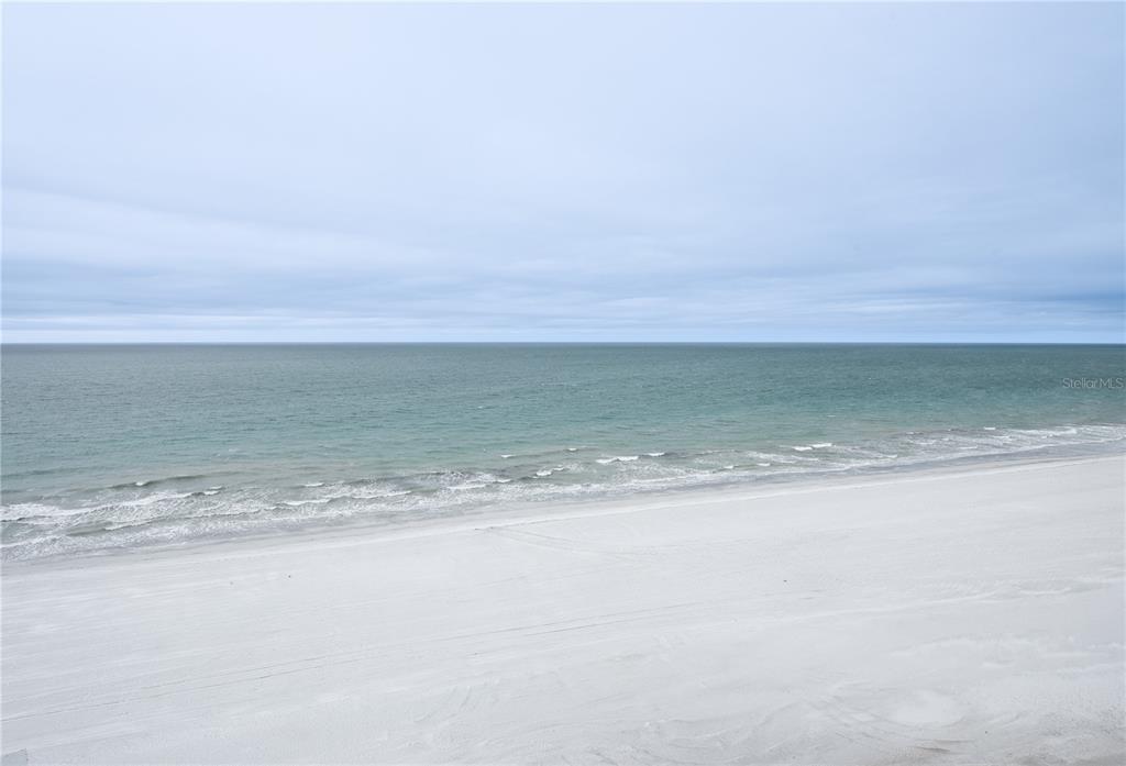A high-angle view of a white sand beach meeting the ocean under a cloudy sky — 1600 GULF BOULEVARD UNIT 1112, CLEARWATER BEACH, FL