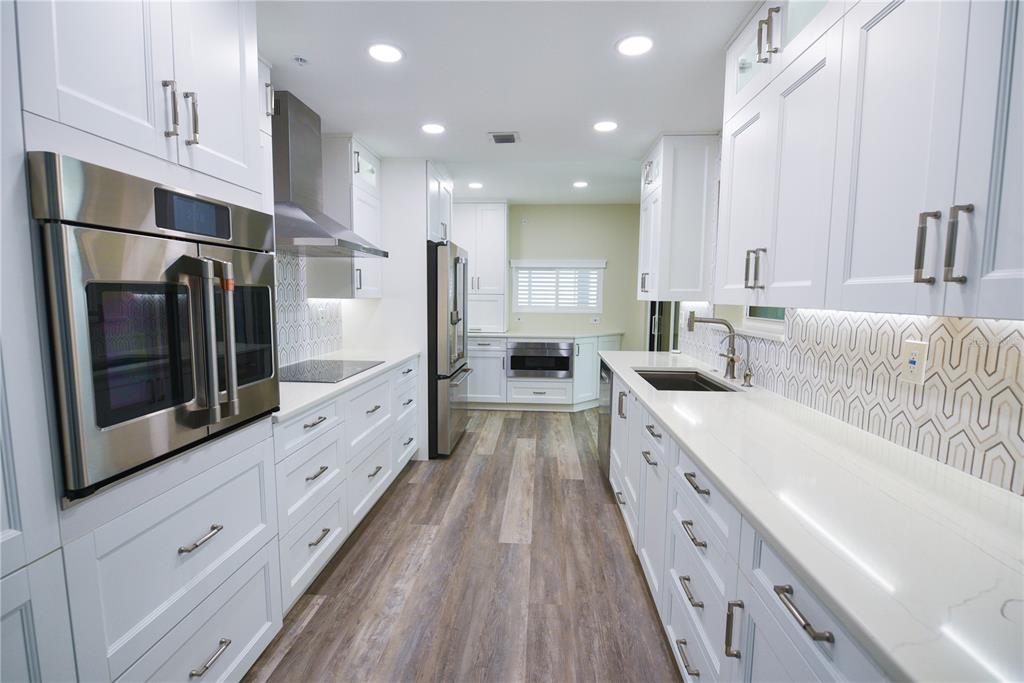 A modern galley kitchen features white cabinetry, stainless steel appliances, and a patterned tile backsplash — 1600 GULF BOULEVARD UNIT 1112, CLEARWATER BEACH, FL
