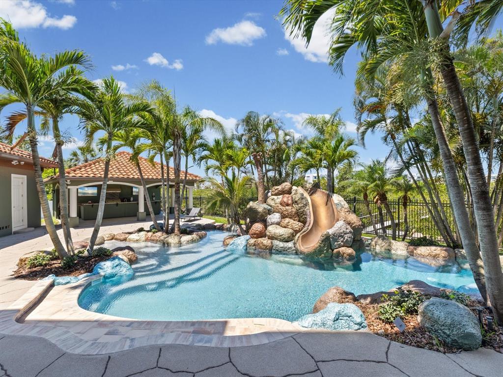 A backyard swimming pool features a rock grotto, a water slide, and a covered patio — 15041 HARDAGE STREET, LARGO, FL
