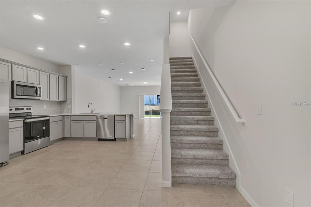 A kitchen with grey cabinets and stainless steel appliances sits beside a carpeted staircase — 2743 FETCHING TRL, DAVENPORT, FL