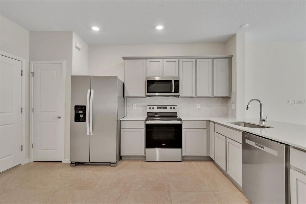 A kitchen features light gray cabinets, stainless steel appliances, white countertops, and tile flooring — 2743 FETCHING TRL, DAVENPORT, FL