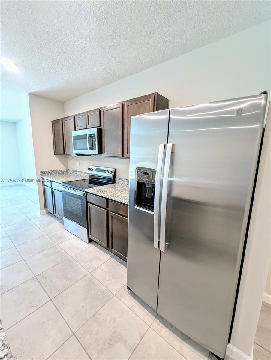 A kitchen features dark wood cabinets, granite countertops, and stainless steel appliances on tiled floors — 285 Raspberry Road # 0, Fort Pierce FL 34981, FORT PIERCE, FL