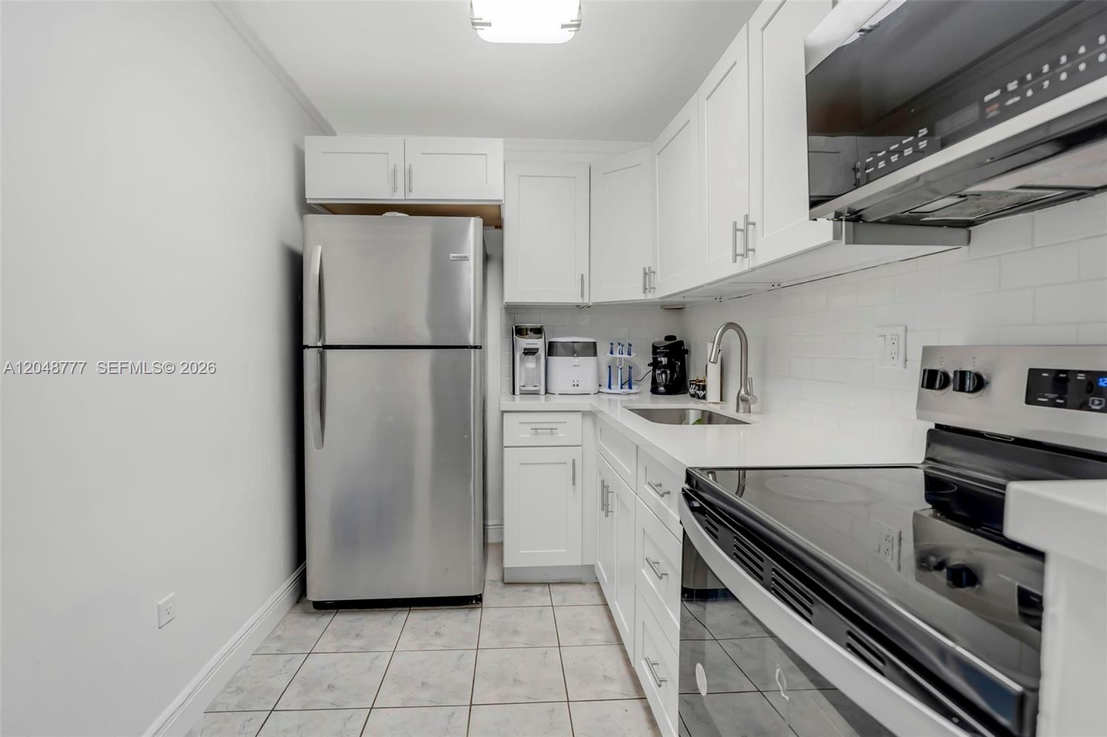 A galley kitchen features white cabinets, stainless steel appliances, and light-colored tile flooring — 8501 NW 8th St # 110, Miami FL 33126, MIAMI, FL