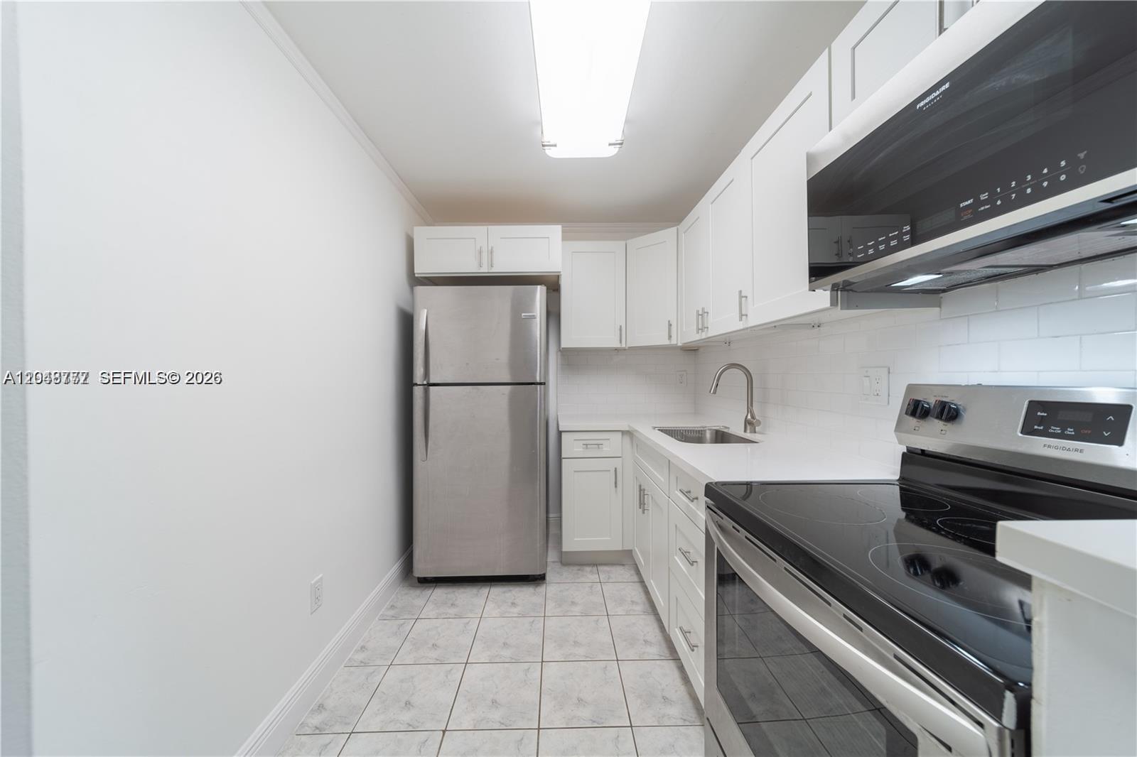 A galley kitchen features white cabinets, stainless steel appliances, white countertops, and tiled flooring — 8501 NW 8th St # 110, Miami FL 33126, MIAMI, FL