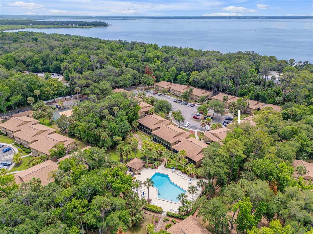An aerial view shows a multi-building apartment complex with a swimming pool and nearby water — 130 JASMINE WOODS COURT UNIT 5B, DELTONA, FL