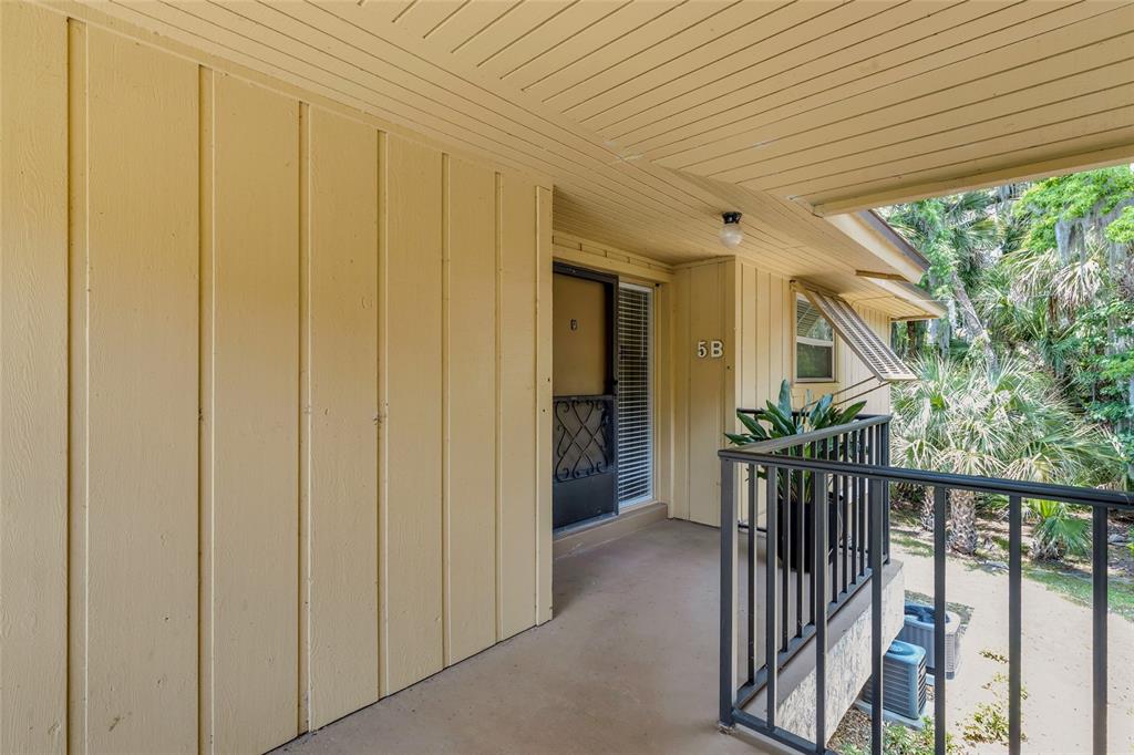 An exterior view of a balcony entrance with yellow vertical siding and a black railing — 130 JASMINE WOODS COURT UNIT 5B, DELTONA, FL