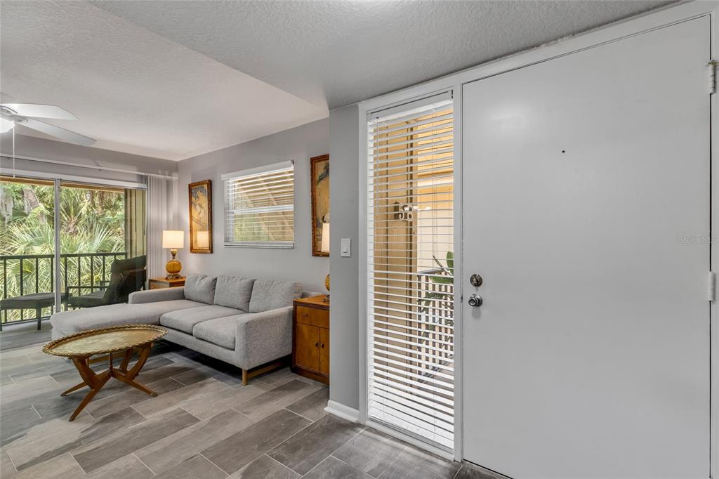 A living room features gray tile flooring, a sectional sofa, and a glass front door — 130 JASMINE WOODS COURT UNIT 5B, DELTONA, FL