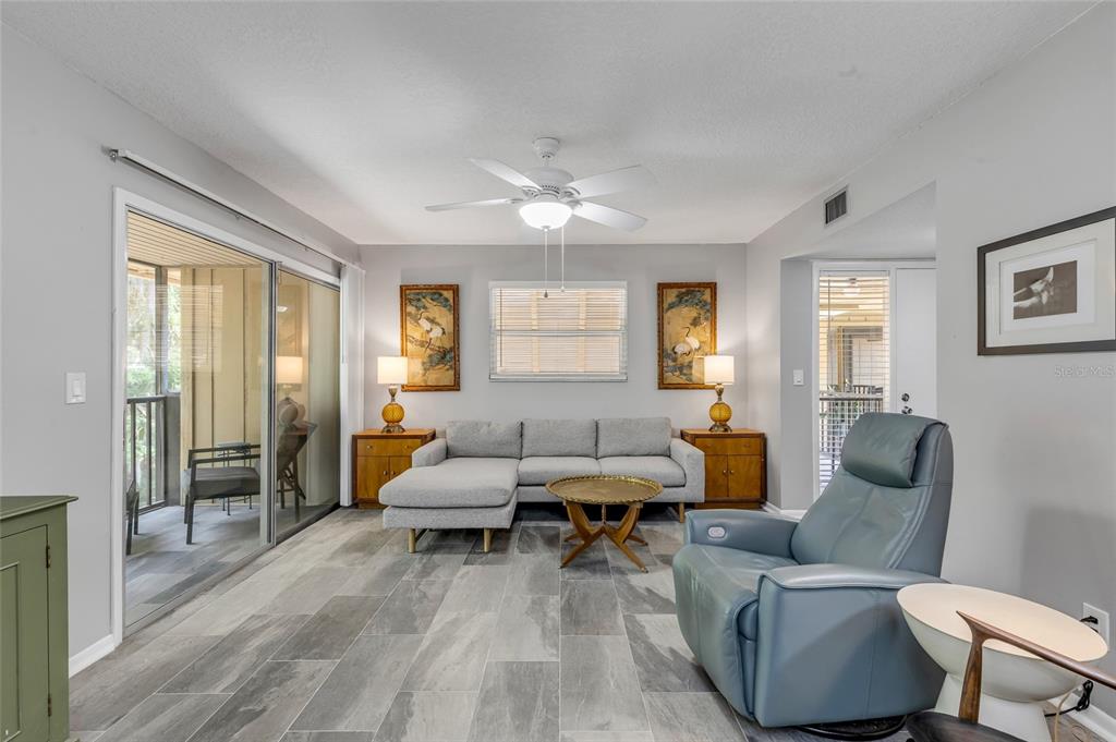 A living room features gray tile flooring, a sectional sofa, and a blue leather recliner — 130 JASMINE WOODS COURT UNIT 5B, DELTONA, FL