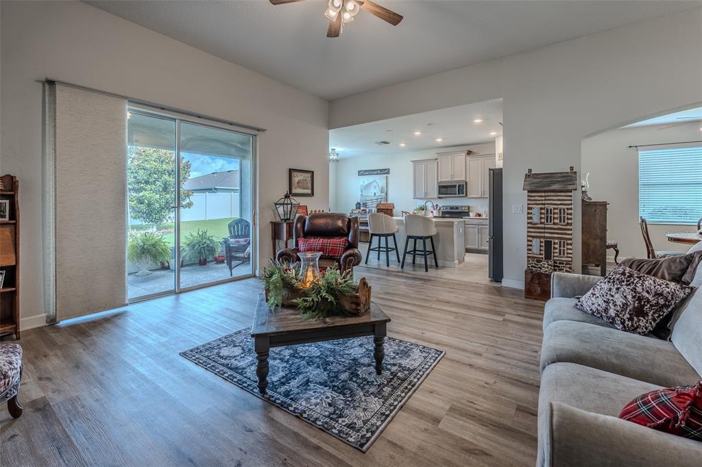 A living room features wood-look flooring, a sliding glass door, and an open kitchen beyond — 9224 SW 60 COURT ROAD, OCALA, FL