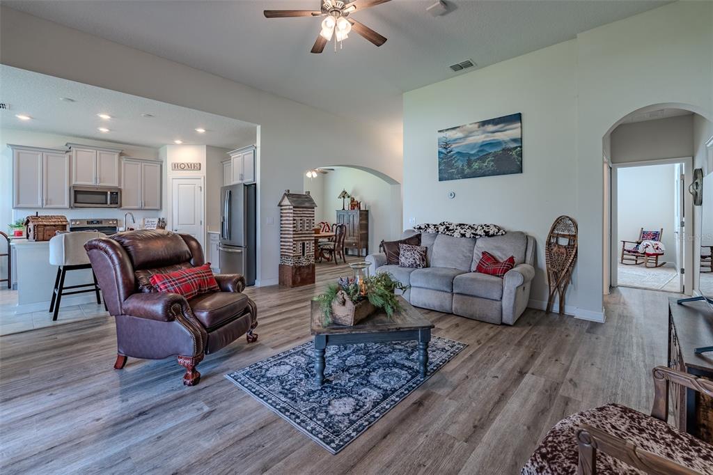 A living room with wood-look flooring, a leather recliner, a grey sofa, and an open kitchen — 9224 SW 60 COURT ROAD, OCALA, FL