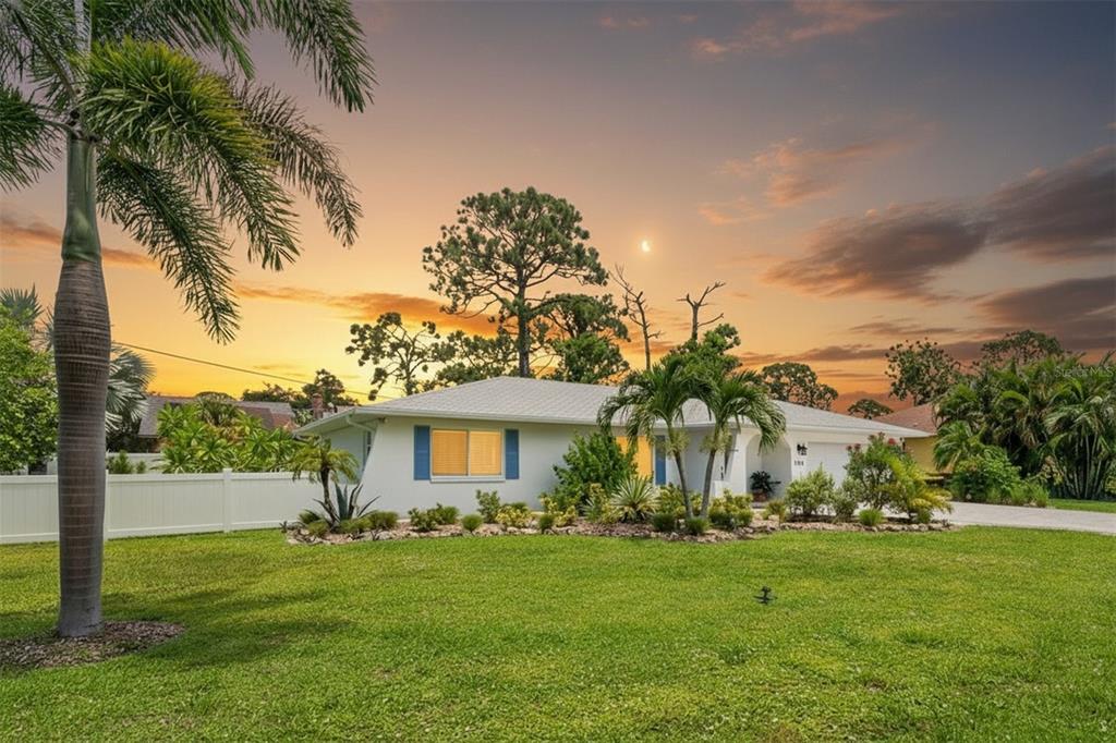 A single-story white house with blue shutters sits behind a green lawn at sunset — 1024 HORIZON ROAD, VENICE, FL