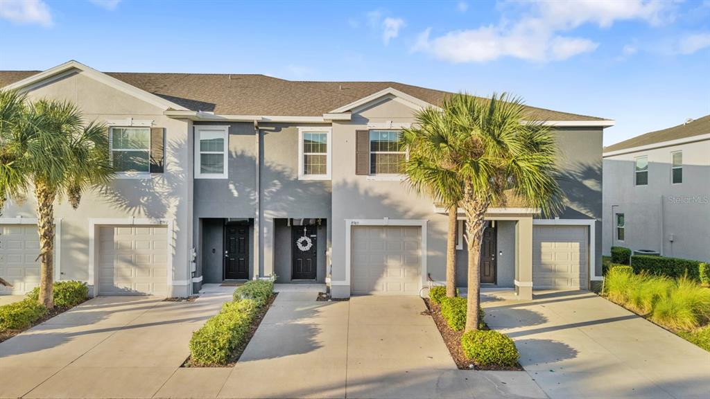 A row of three-story townhomes with gray stucco facades, attached garages, and palm trees — 8965 INDIGO TRAIL LOOP, RIVERVIEW, FL
