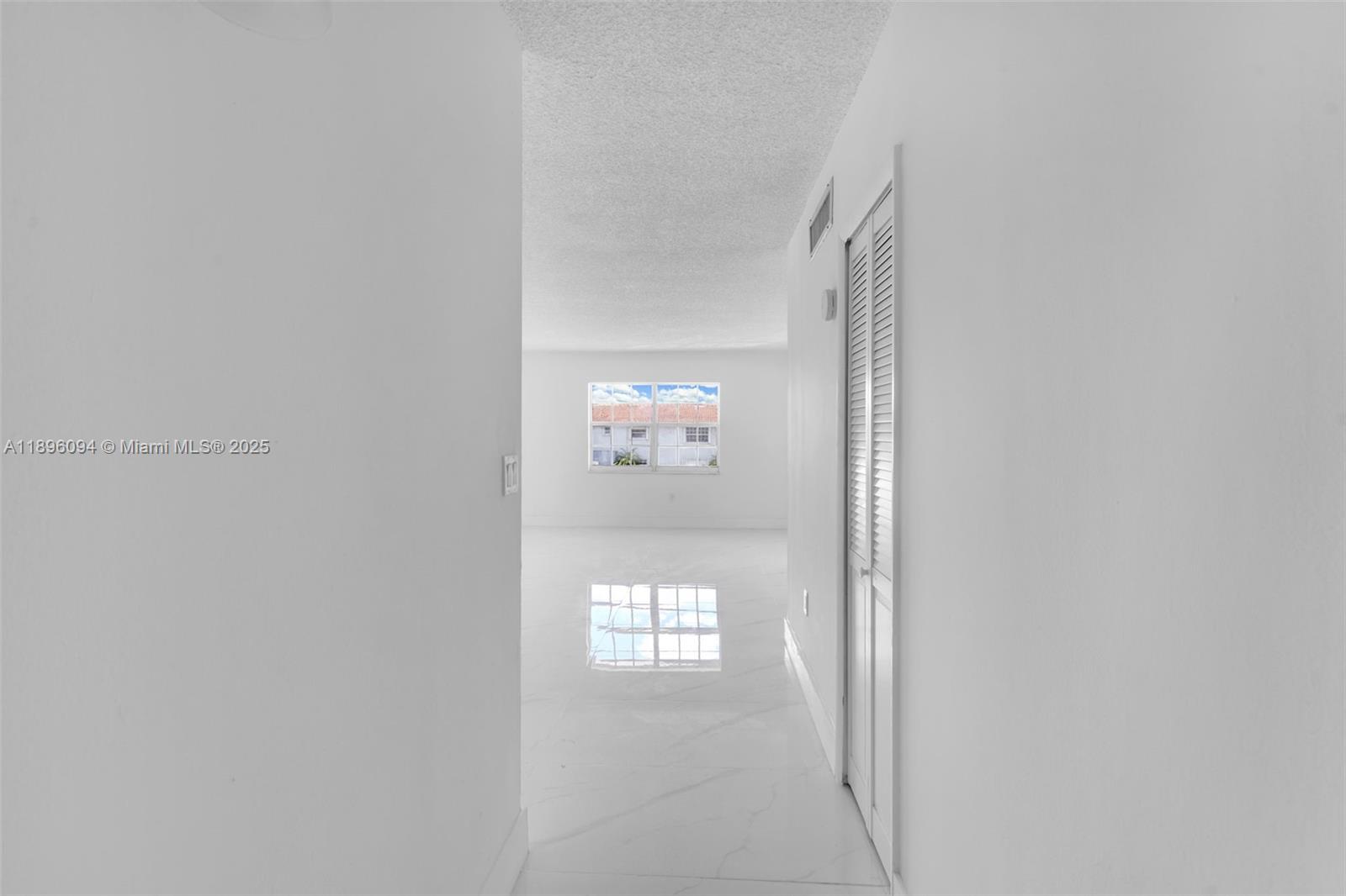 A white hallway with tile flooring leads toward a bright room with a window — 4050 NW 135th St # 11, Opa-Locka FL 33054, OPA-LOCKA, FL