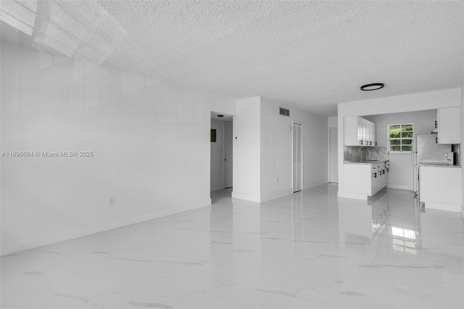 An open-concept living area features white walls, glossy tile flooring, and an adjacent kitchen — 4050 NW 135th St # 11, Opa-Locka FL 33054, OPA-LOCKA, FL
