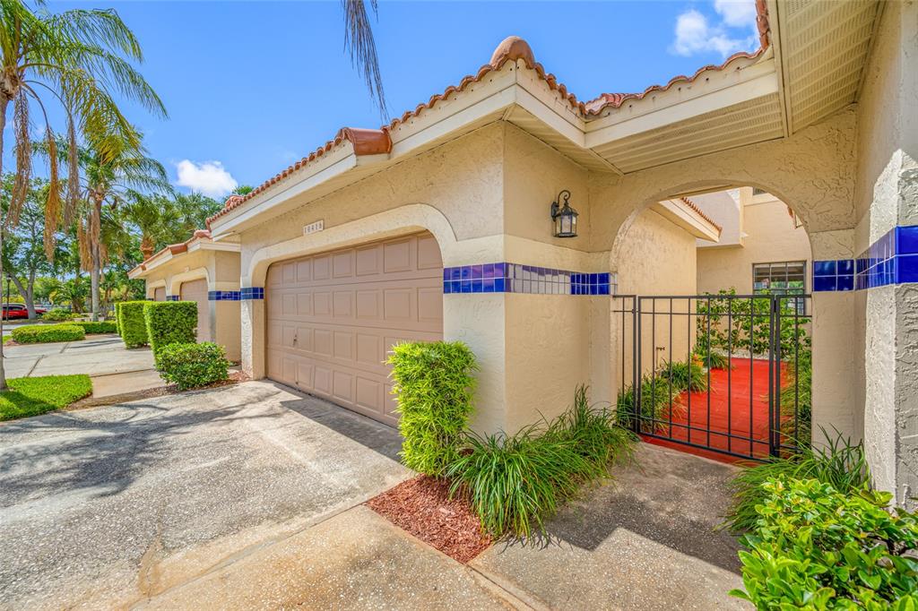 A beige house exterior features a garage, a gated courtyard entrance, and blue tile accents — 10416 SAINT TROPEZ PLACE, TAMPA, FL