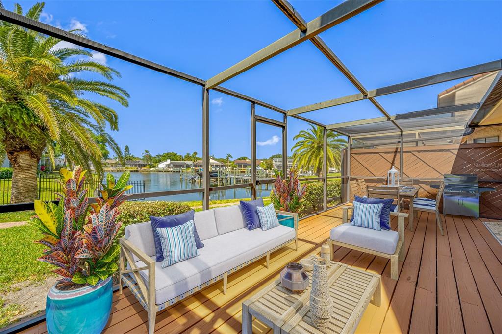 A screened-in wooden deck features outdoor furniture, a grill, and a view of a canal — 10416 SAINT TROPEZ PLACE, TAMPA, FL