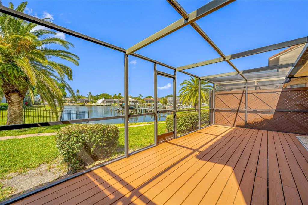 A screened-in wooden deck overlooks a canal with palm trees and neighboring houses — 10416 SAINT TROPEZ PLACE, TAMPA, FL
