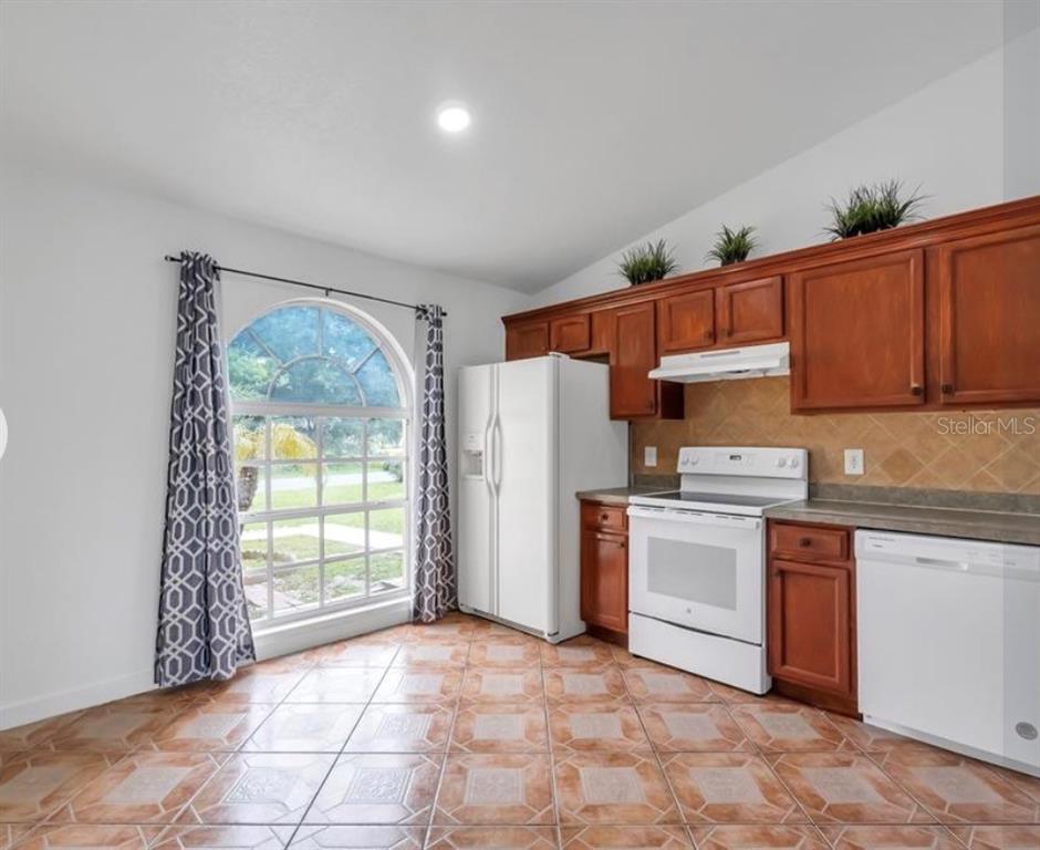 A kitchen with wood cabinets, white appliances, tile flooring, and a large arched window — 34 BRADFORD, KISSIMMEE, FL