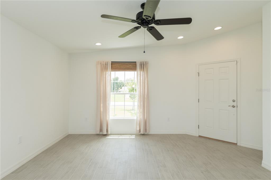 A bright room with white walls, light wood-look tile flooring, a ceiling fan, and a door — 3512 ELLIOTT PLACE, BARTOW, FL