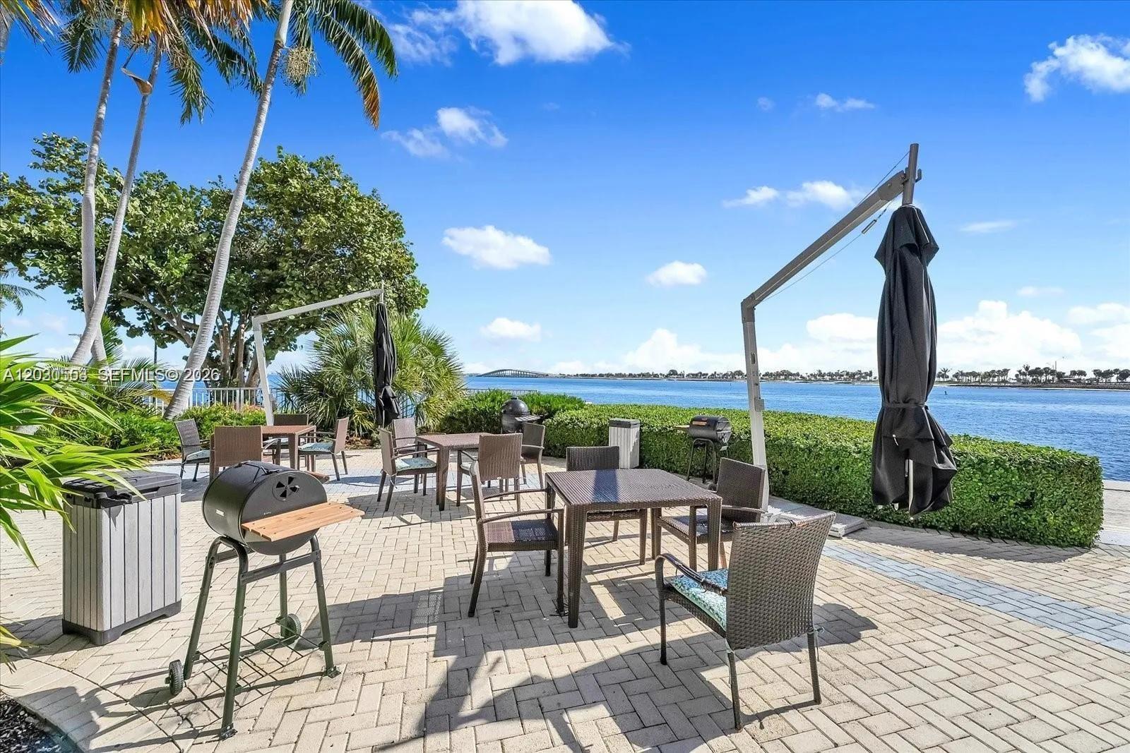 An outdoor patio features dining tables, chairs, and charcoal grills overlooking a waterfront view — 2451 Brickell Ave # 5G, Miami FL 33129, MIAMI, FL