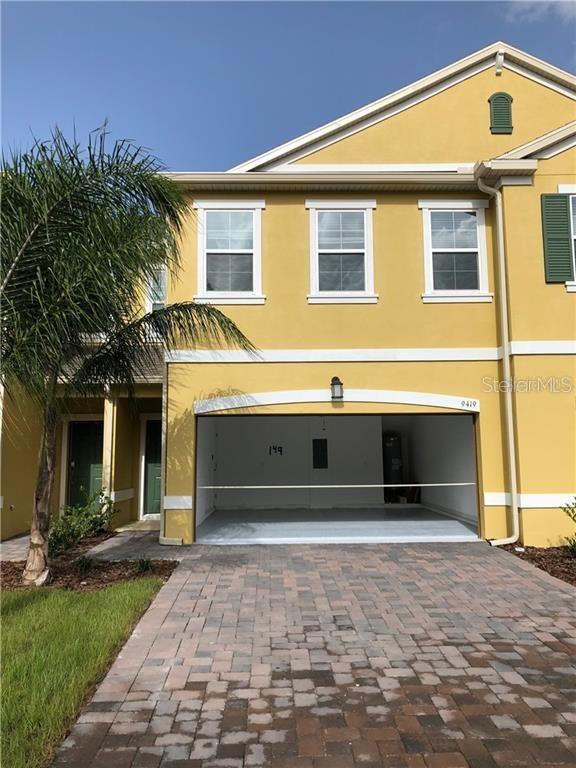 The exterior of a yellow two-story townhouse features a paved driveway and an open garage — 9419 TECUMSEH DRIVE, ALAFAYA, FL