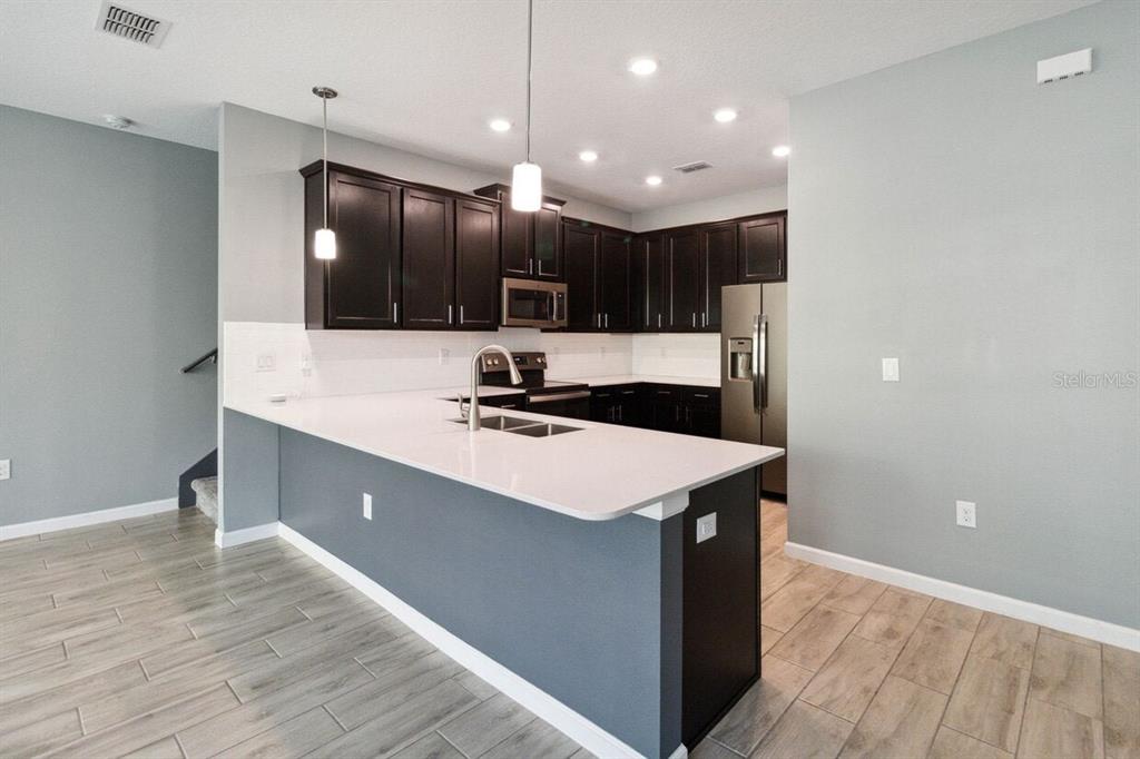 A modern kitchen features dark wood cabinets, white countertops, and a large breakfast bar island — 9419 TECUMSEH DRIVE, ALAFAYA, FL