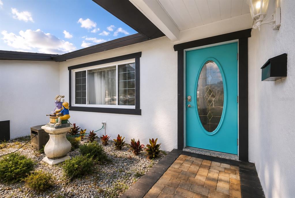 The exterior of a home features a bright turquoise front door and a stone walkway — 6745 RALSTON BEACH CIRCLE, TAMPA, FL