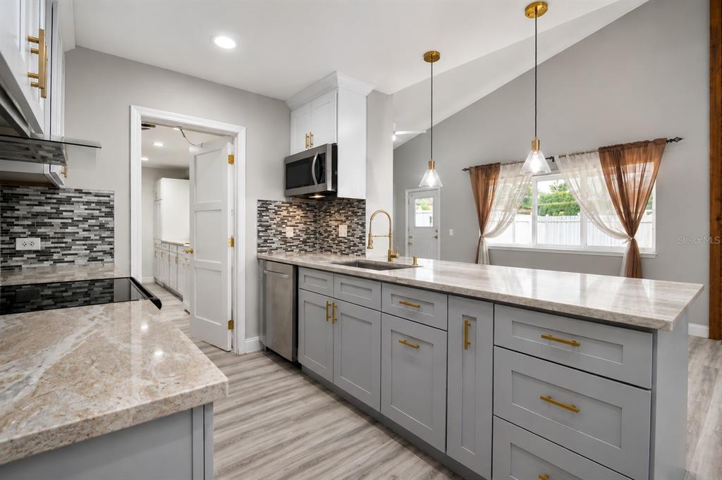 A kitchen with gray cabinets, stone countertops, a tile backsplash, and two hanging pendant lights — 6745 RALSTON BEACH CIRCLE, TAMPA, FL