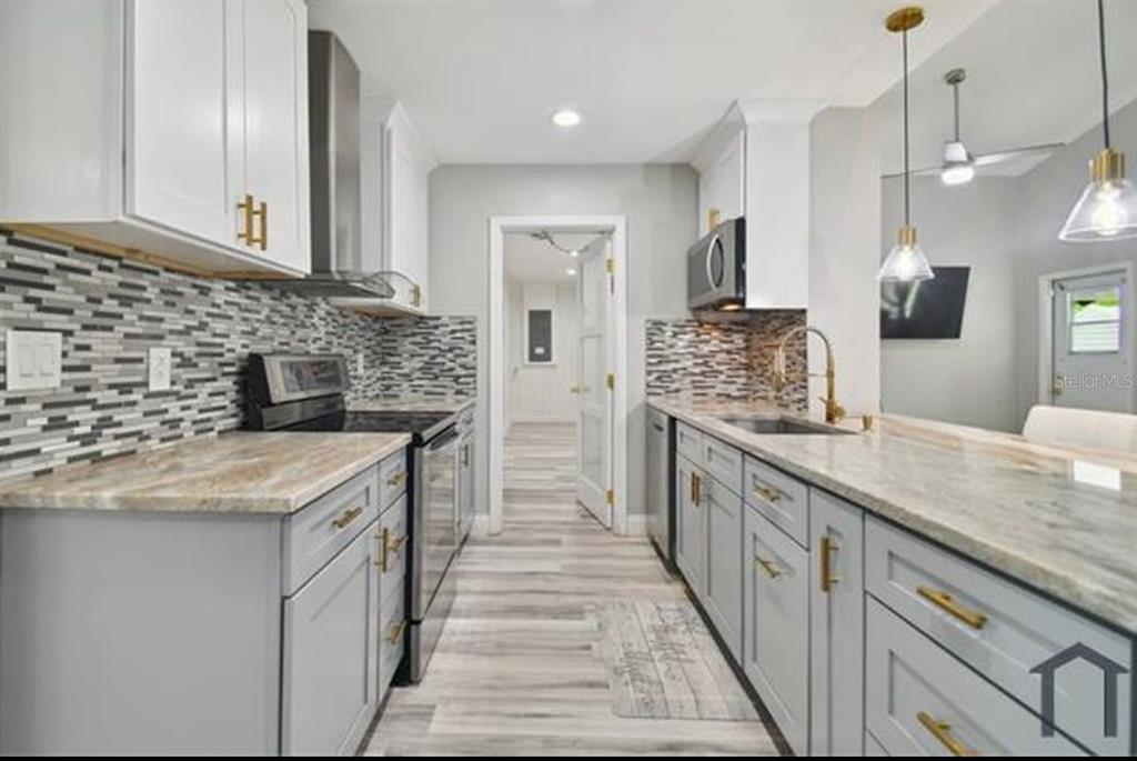 A kitchen with gray lower cabinets, white upper cabinets, stone countertops, and a tiled backsplash — 6745 RALSTON BEACH CIRCLE, TAMPA, FL