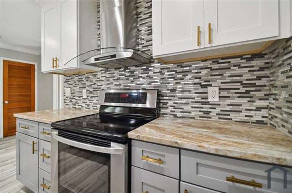A kitchen features grey cabinets, marble-look countertops, a mosaic tile backsplash, and stainless steel appliances — 6745 RALSTON BEACH CIRCLE, TAMPA, FL