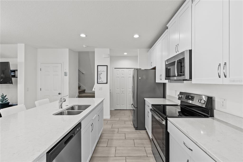 A modern kitchen features white cabinets, quartz countertops, stainless steel appliances, and tile flooring — 1286 WISPY CYPRESS DRIVE, KISSIMMEE, FL