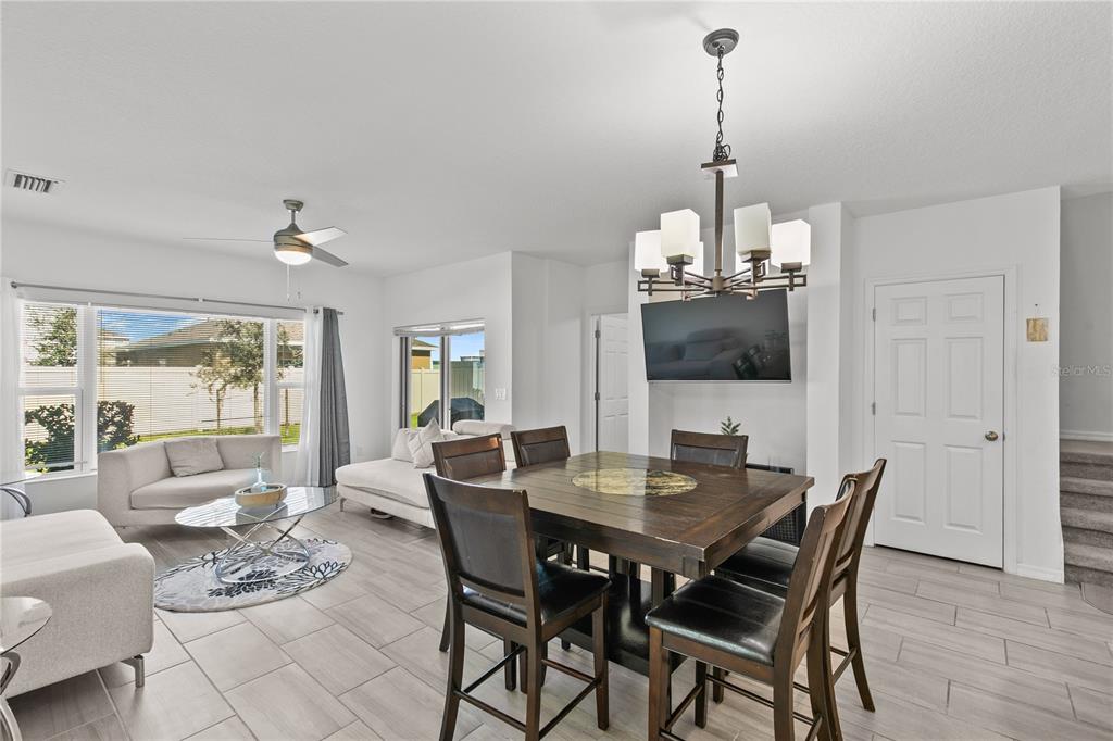 A dining area with a dark wood table and chandelier adjacent to a living room — 1286 WISPY CYPRESS DRIVE, KISSIMMEE, FL