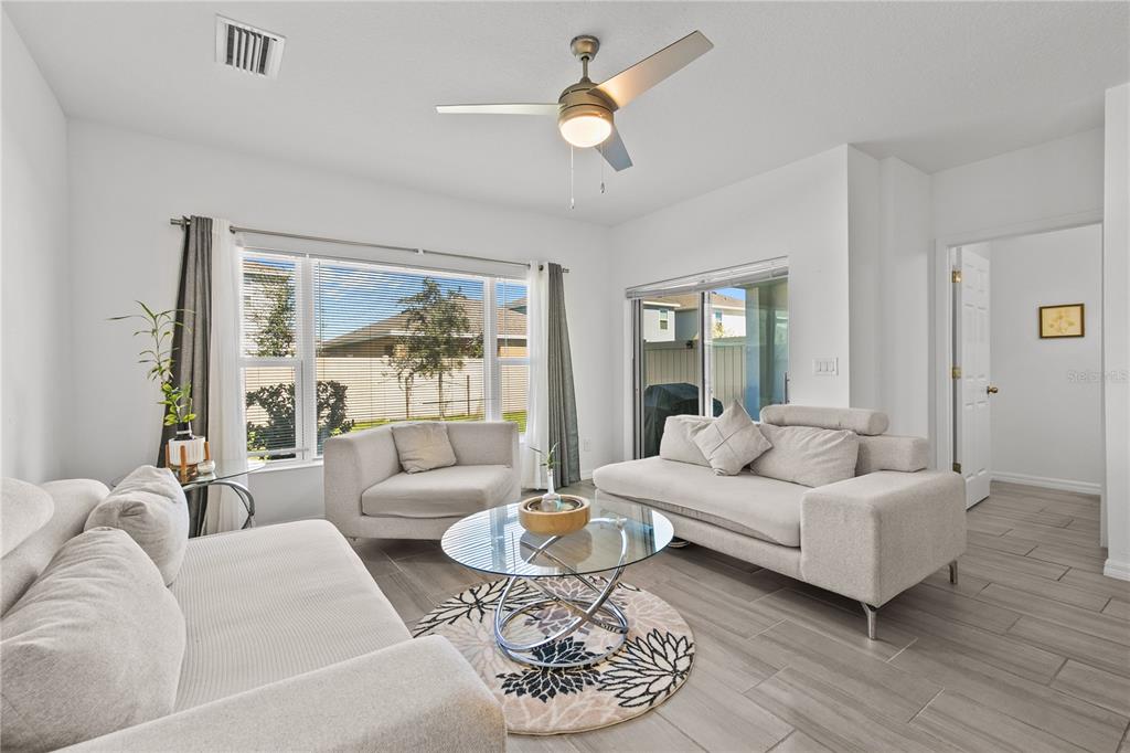 A bright living room features light-colored sofas, a glass coffee table, and tile flooring — 1286 WISPY CYPRESS DRIVE, KISSIMMEE, FL
