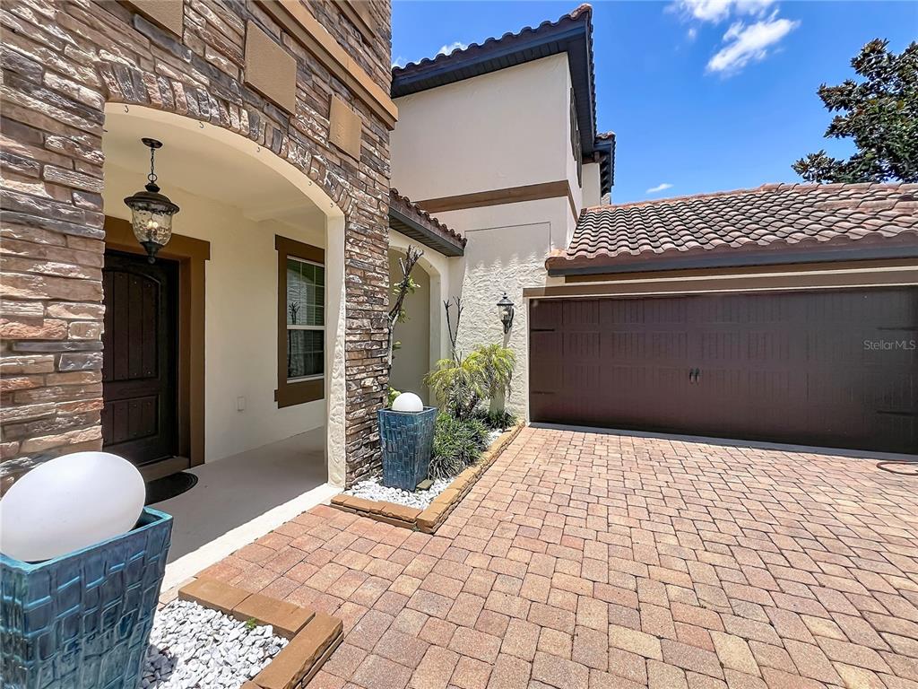 A stone-accented home exterior features a covered entryway, a brown garage door, and paver driveway — 8316 LOOKOUT POINTE DRIVE, WINDERMERE, FL